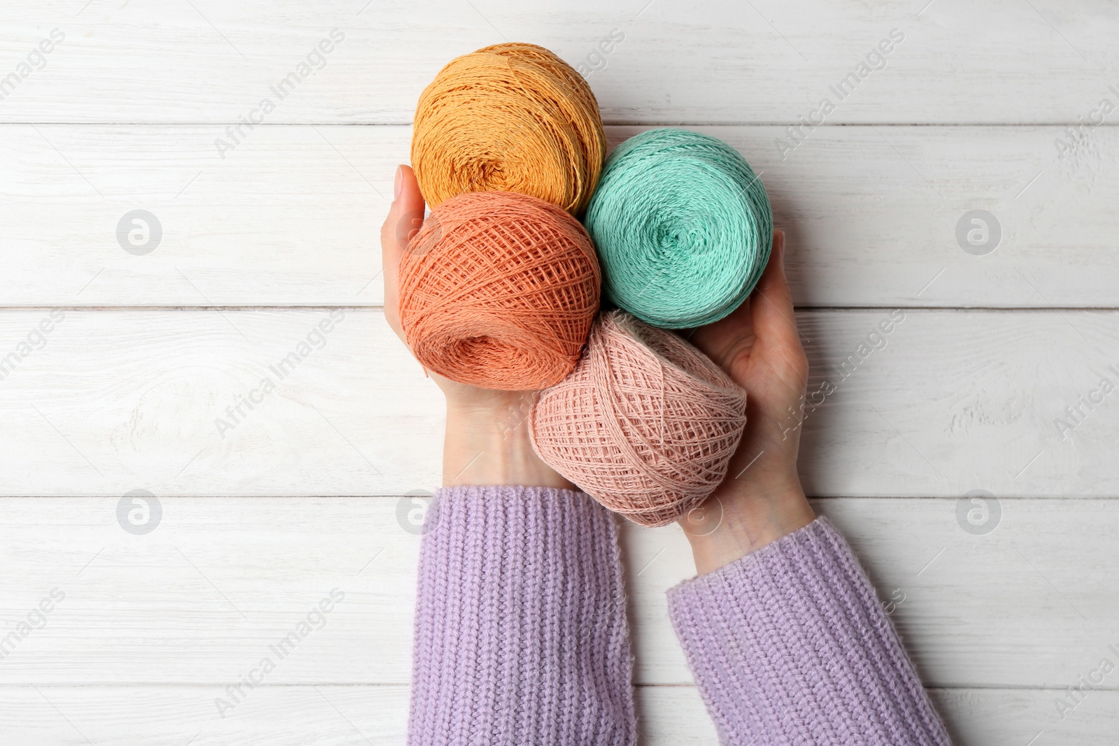 Photo of Woman holding clews of threads on wooden background, top view