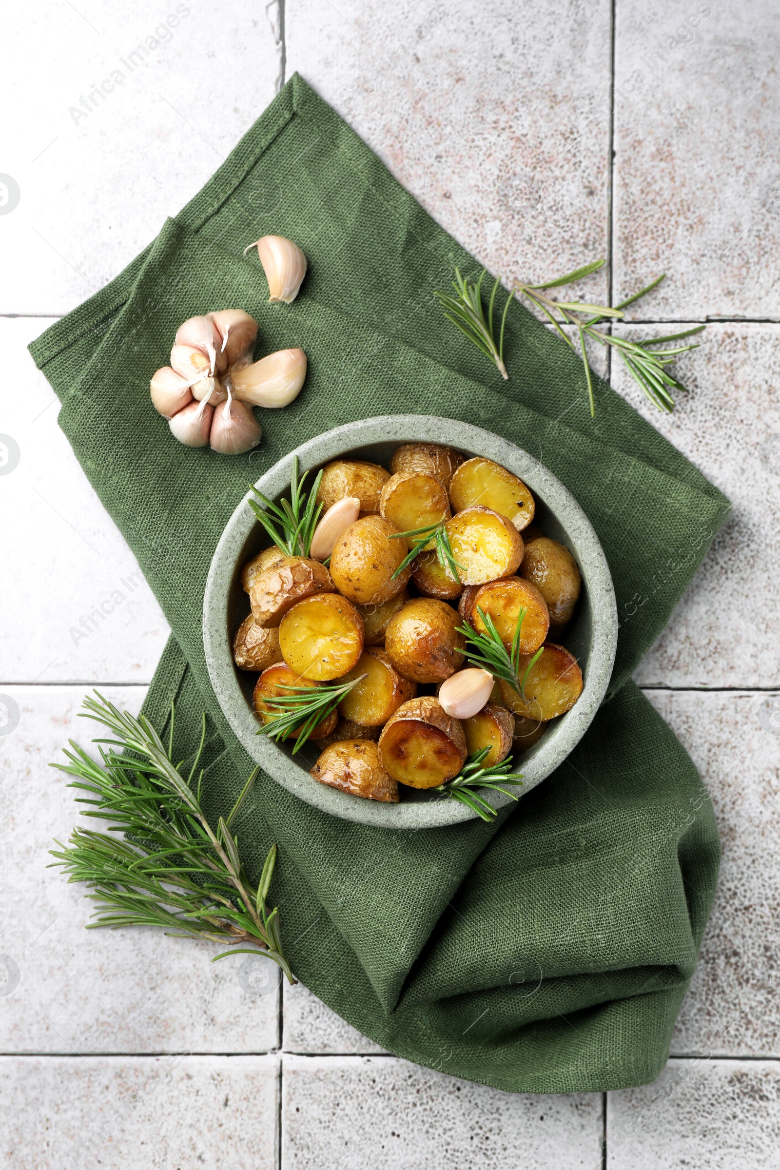 Photo of Bowl with tasty baked potato and aromatic rosemary on light tiled table, flat lay