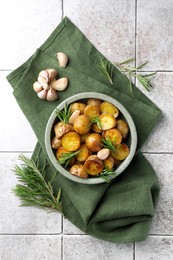 Bowl with tasty baked potato and aromatic rosemary on light tiled table, flat lay