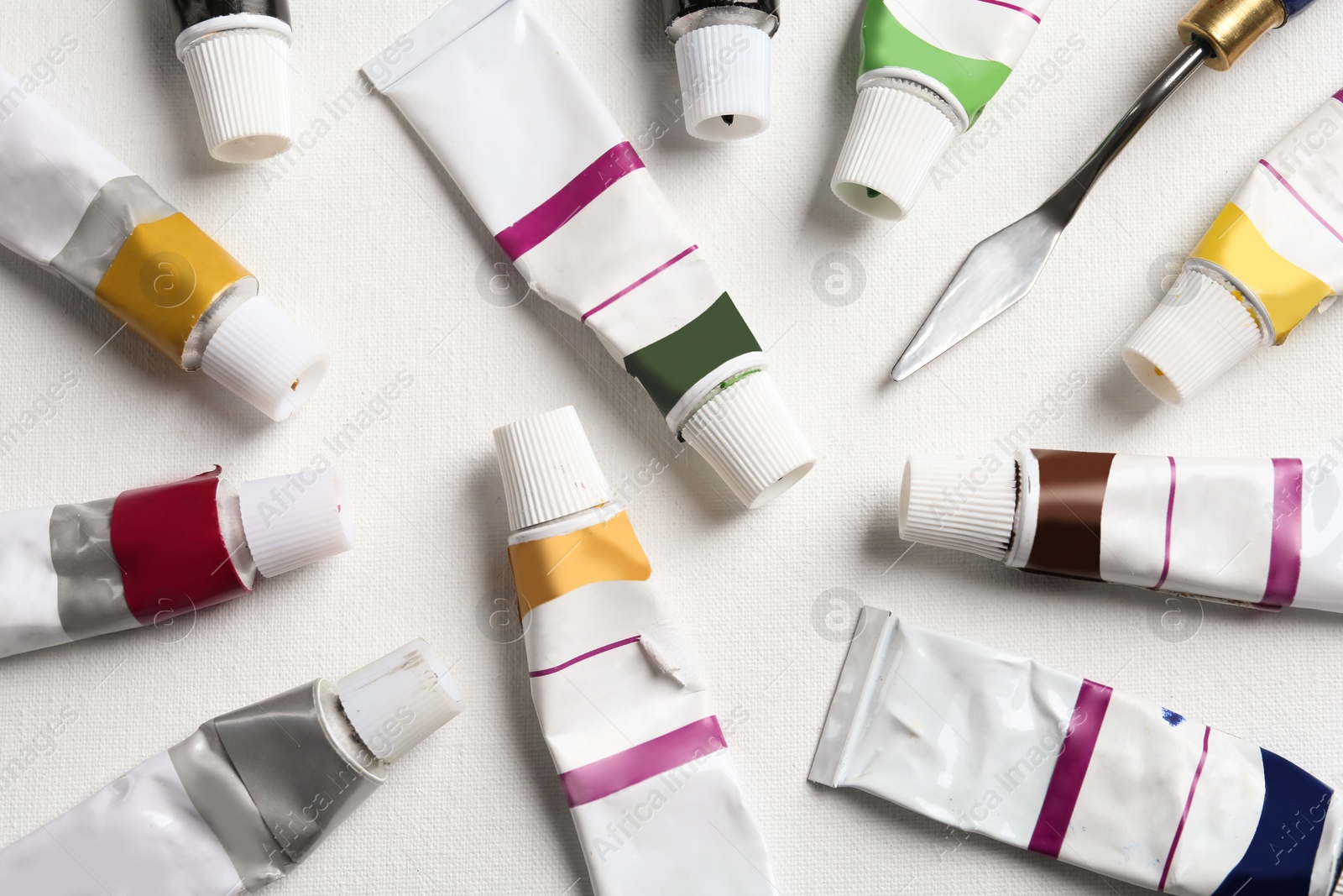 Photo of Tubes with paints and spatula on blank canvas, flat lay