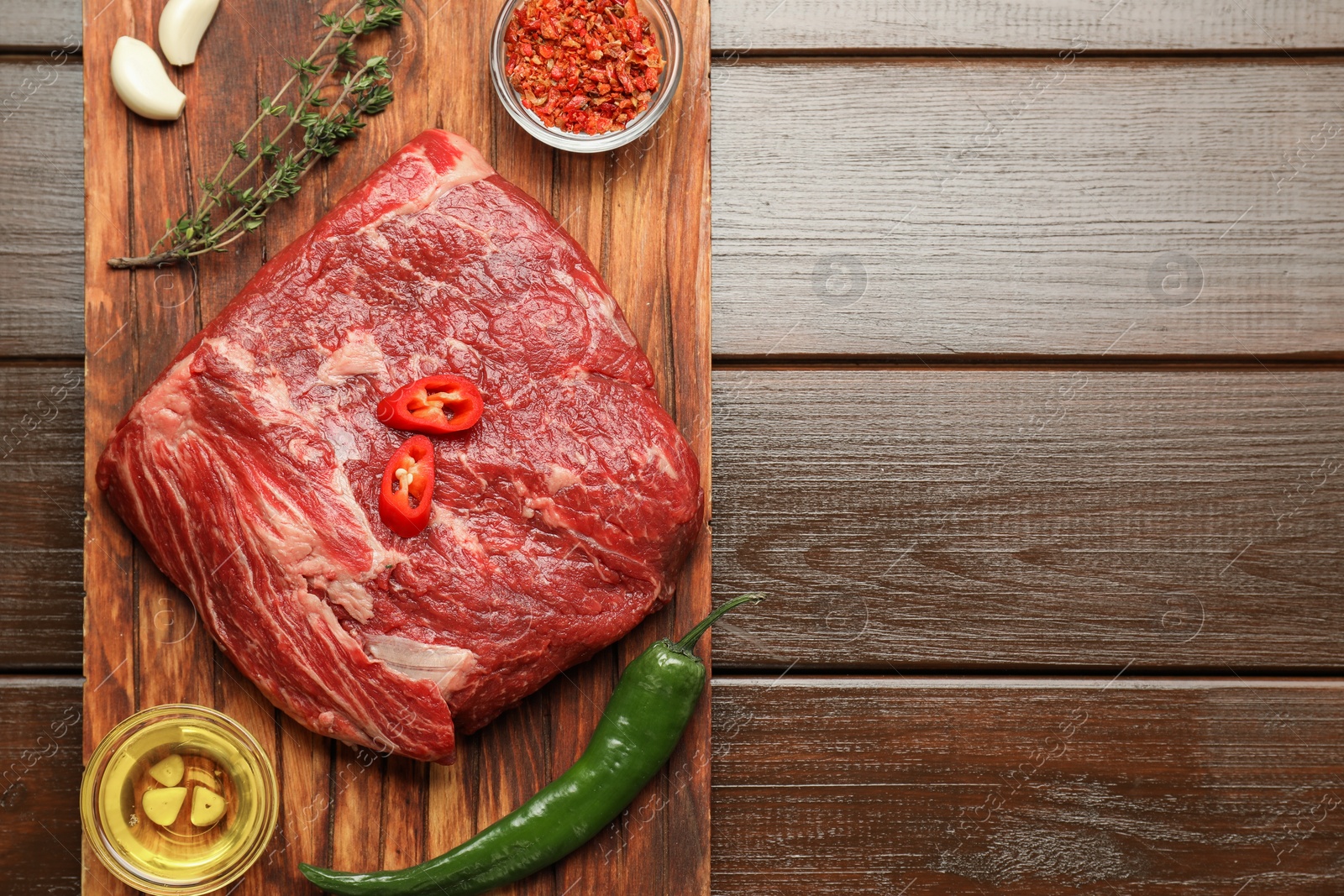 Photo of Fresh raw beef cut, spices and oil on wooden table, top view. Space for text