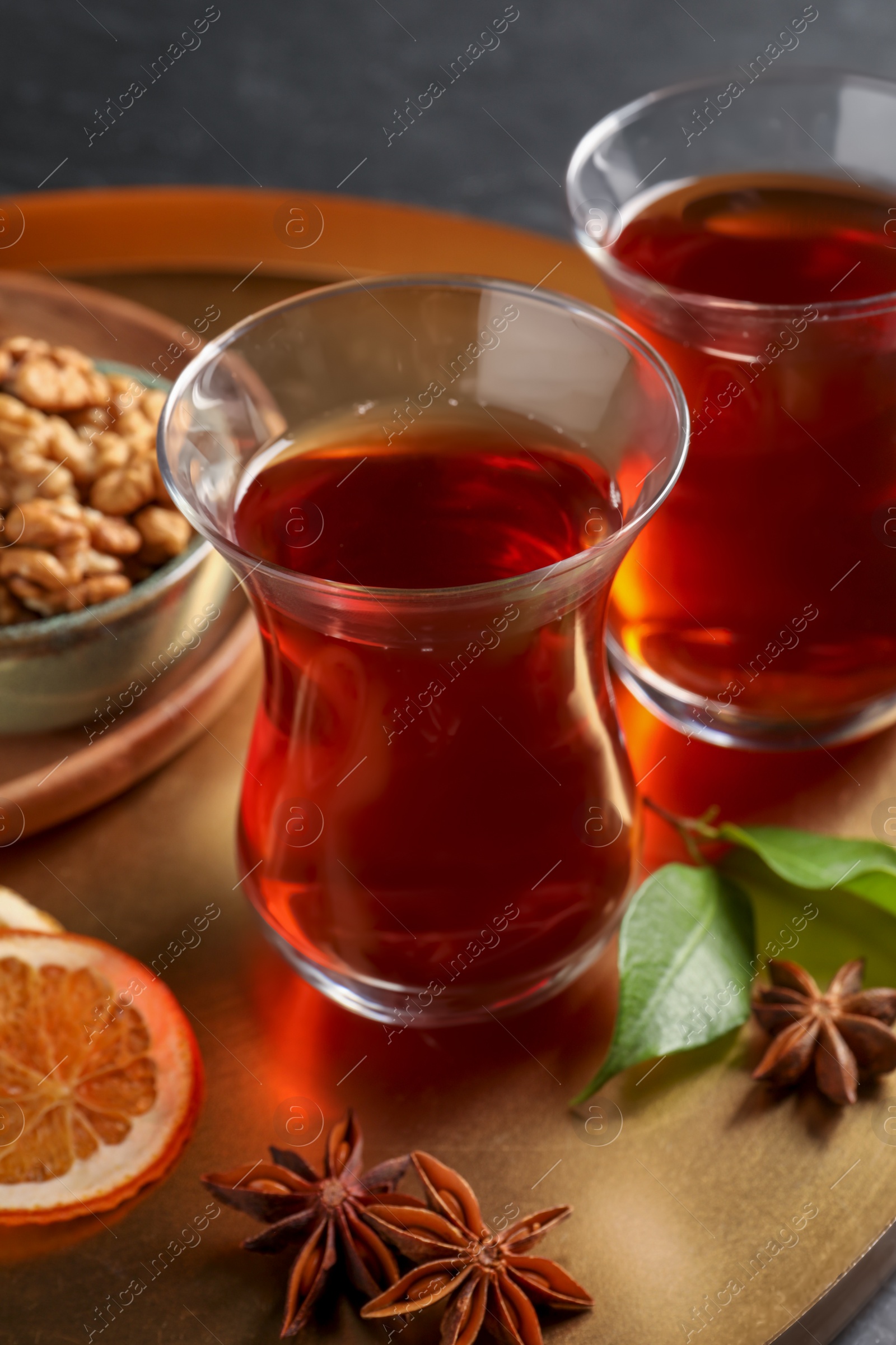 Photo of Tray with glasses of traditional Turkish tea, walnuts, dried orange and anise on table, closeup