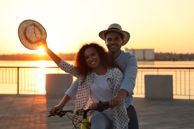 Photo of Young couple riding bicycle on city waterfront at sunset