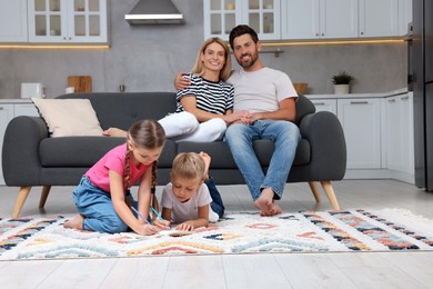 Photo of Happy couple spending time together while their children drawing on floor at home