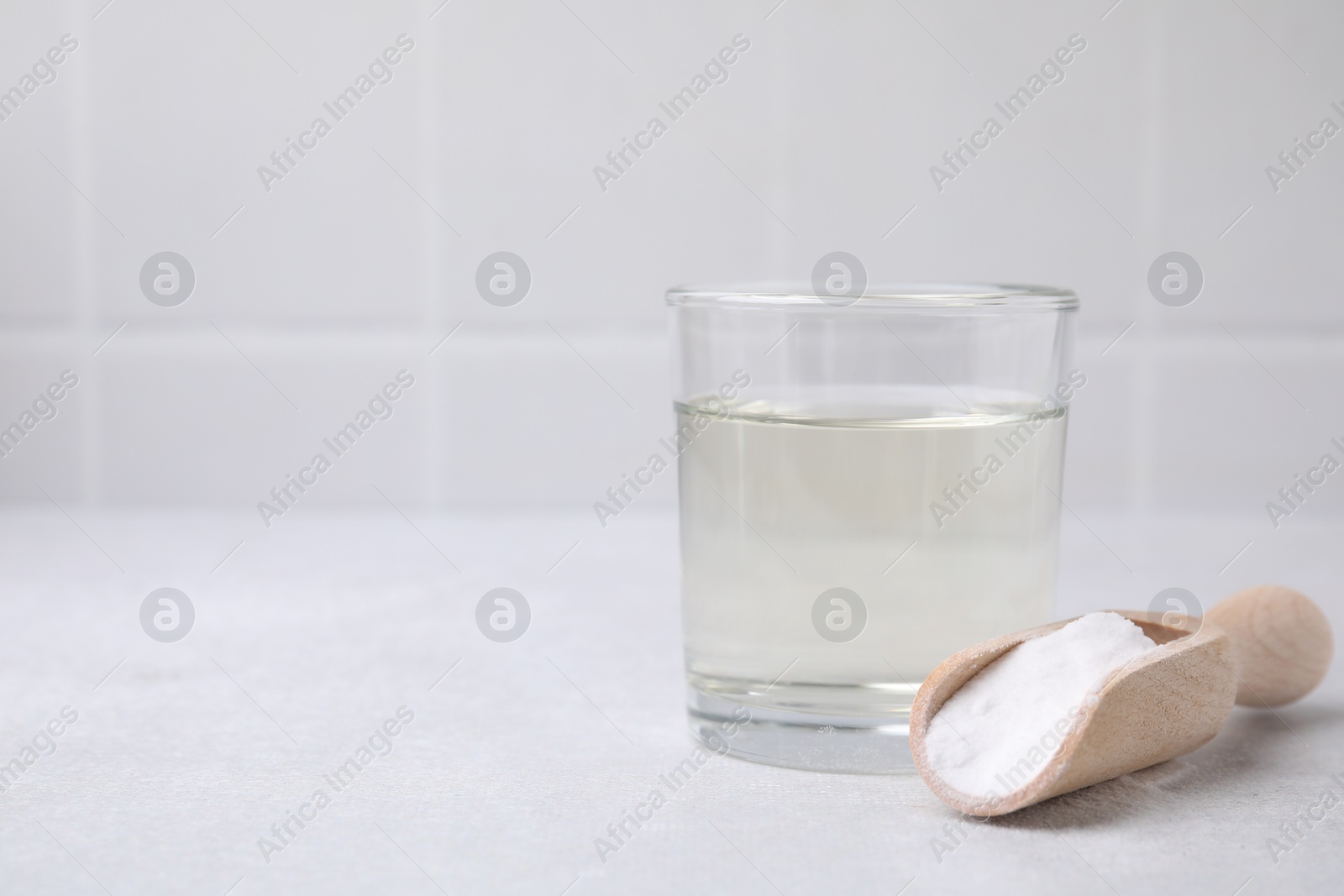 Photo of Vinegar in glass, baking soda and wooden scoop on light table, space for text