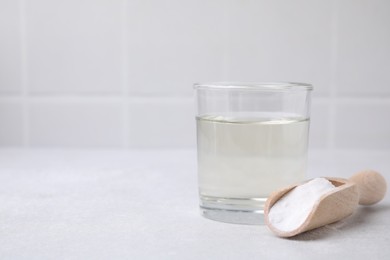 Photo of Vinegar in glass, baking soda and wooden scoop on light table, space for text