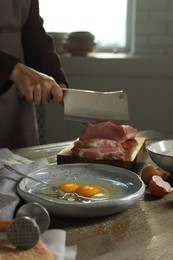 Woman cooking schnitzel at wooden table indoors, selective focus