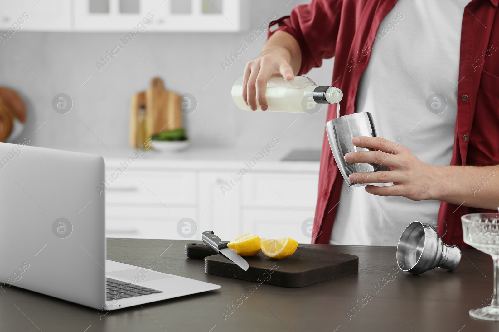 Photo of Man learning to make cocktail with online video on laptop at table in kitchen, closeup. Time for hobby