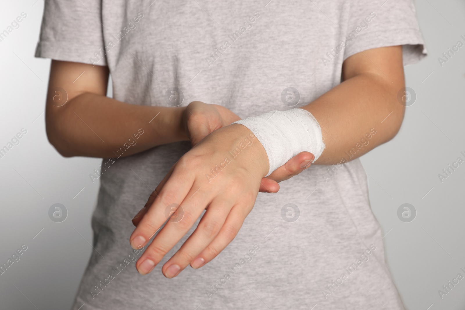 Photo of Woman with wrist wrapped in medical bandage on light grey background, closeup