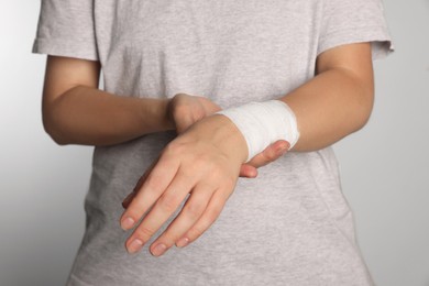 Photo of Woman with wrist wrapped in medical bandage on light grey background, closeup