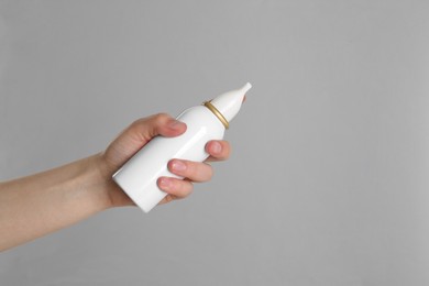Photo of Woman holding nasal spray on grey background, closeup. Space for text