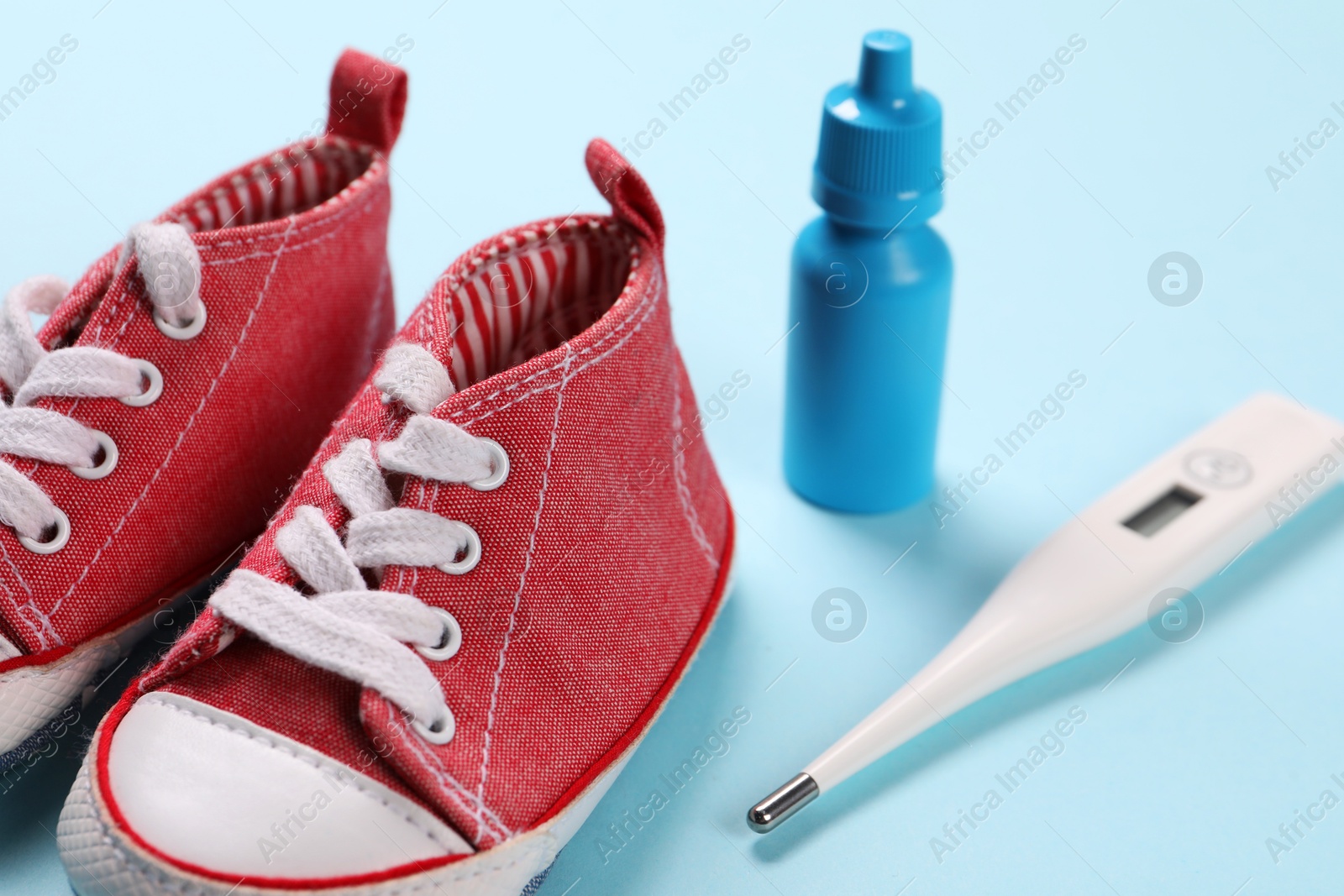 Photo of Kid's sneakers, thermometer and nasal spray on light blue background, closeup