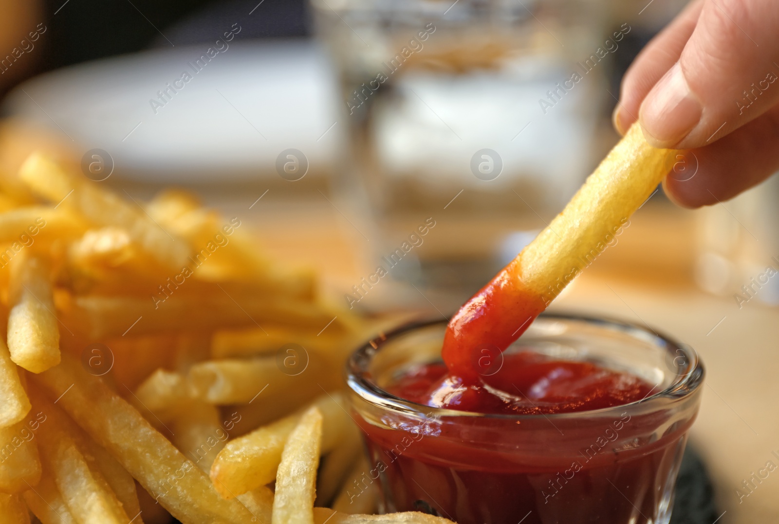 Photo of Woman dipping French fries into red sauce in cafe, closeup