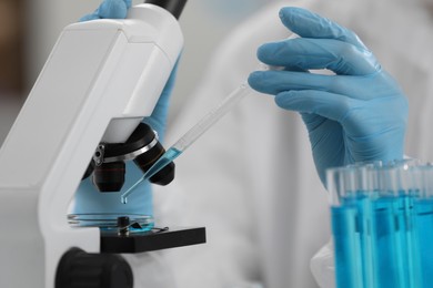 Photo of Scientist dripping sample onto Petri dish while working with microscope in laboratory, closeup