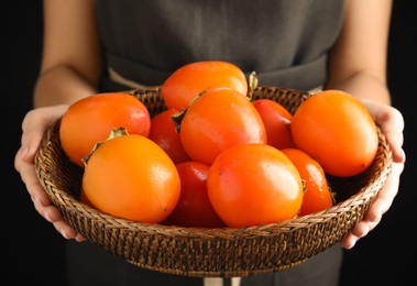 Photo of Woman holding delicious fresh persimmons on black background, closeup