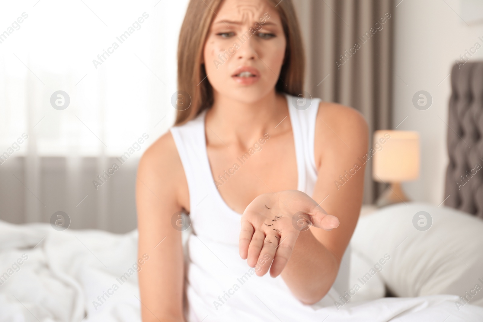 Photo of Emotional young woman holding fallen eyelashes indoors