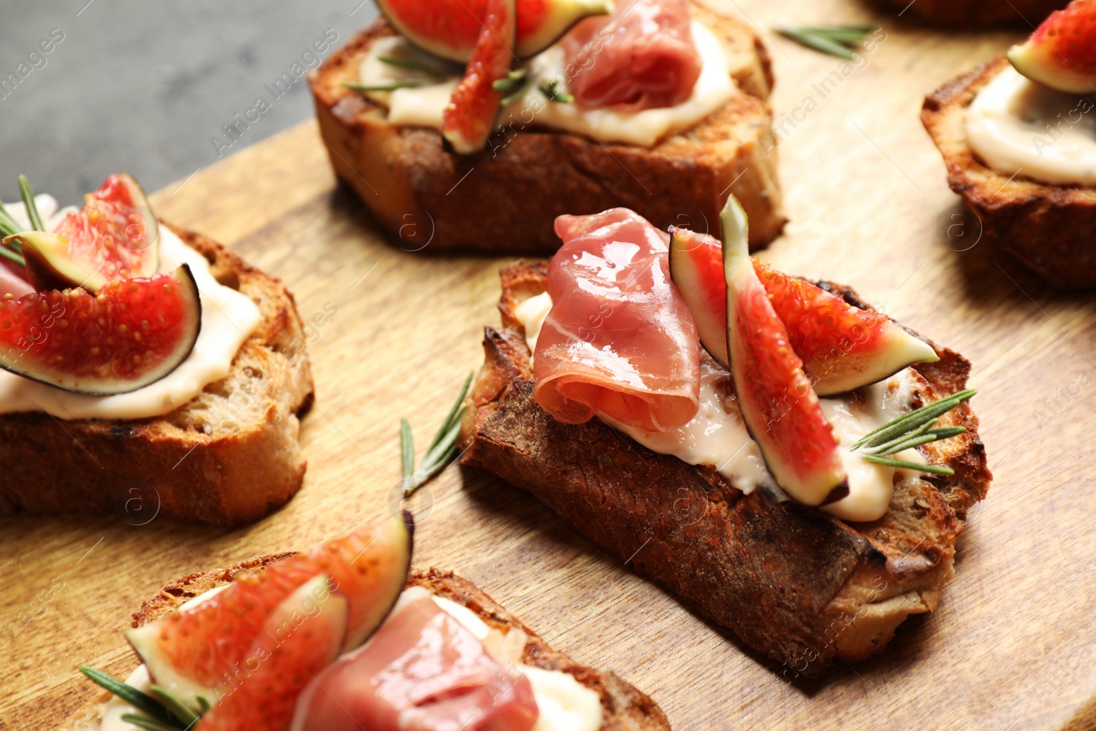 Photo of Bruschettas with cream cheese, prosciutto and figs served on wooden board, closeup