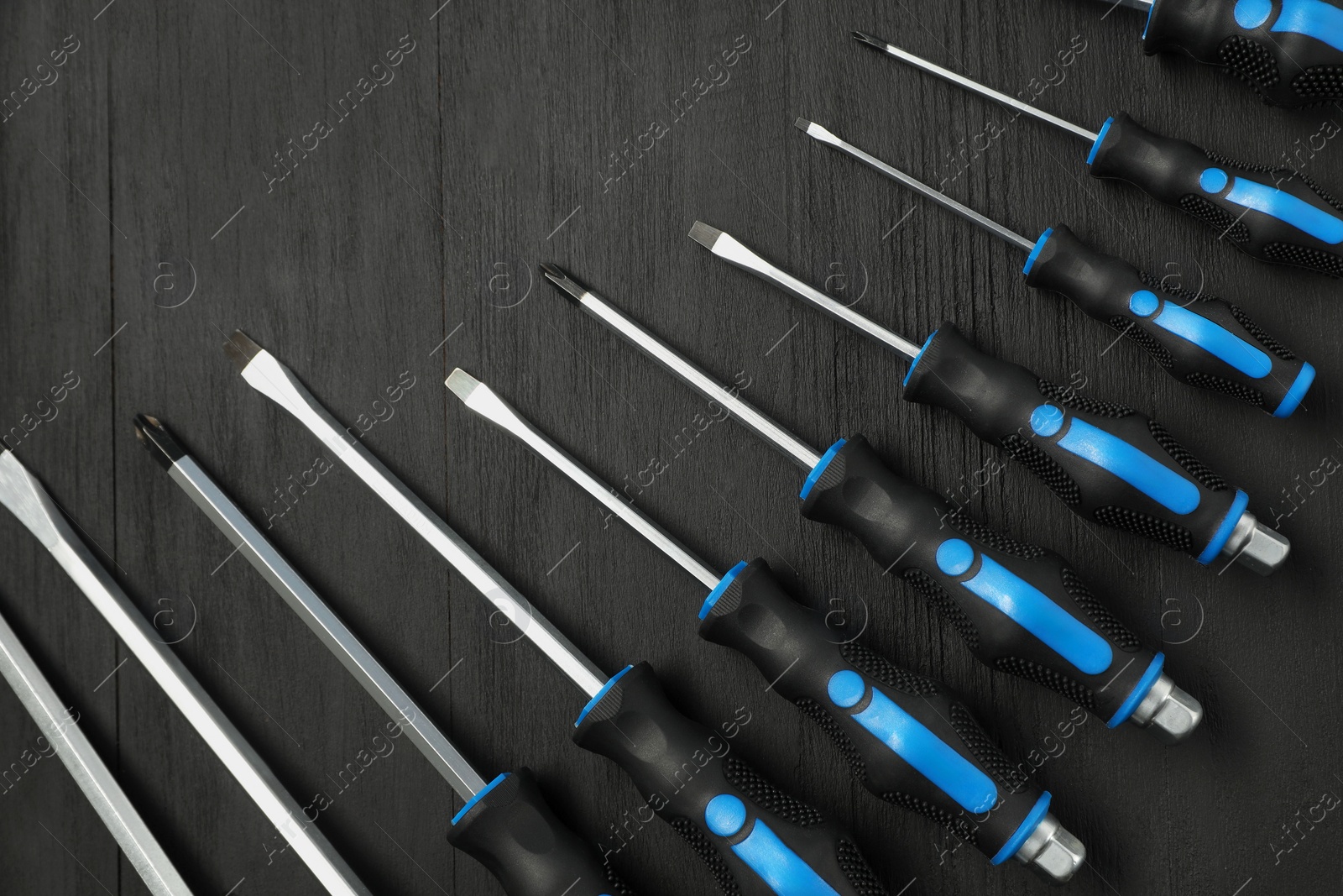 Photo of Set of screwdrivers on black wooden table, top view