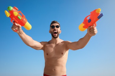 Photo of Man with water guns having fun against blue sky, low angle view