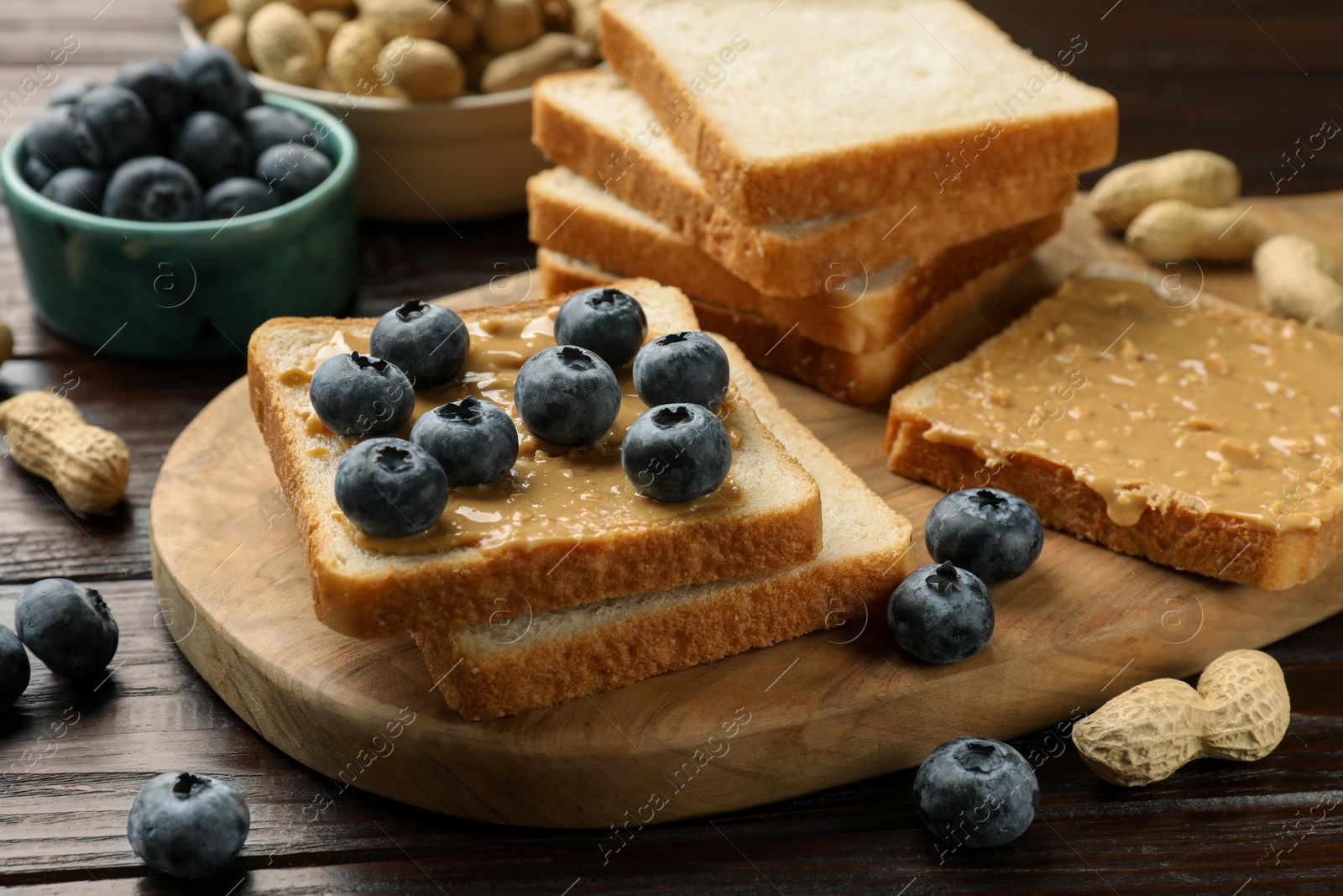 Photo of Delicious toasts with peanut butter, blueberries and nuts on wooden table, closeup