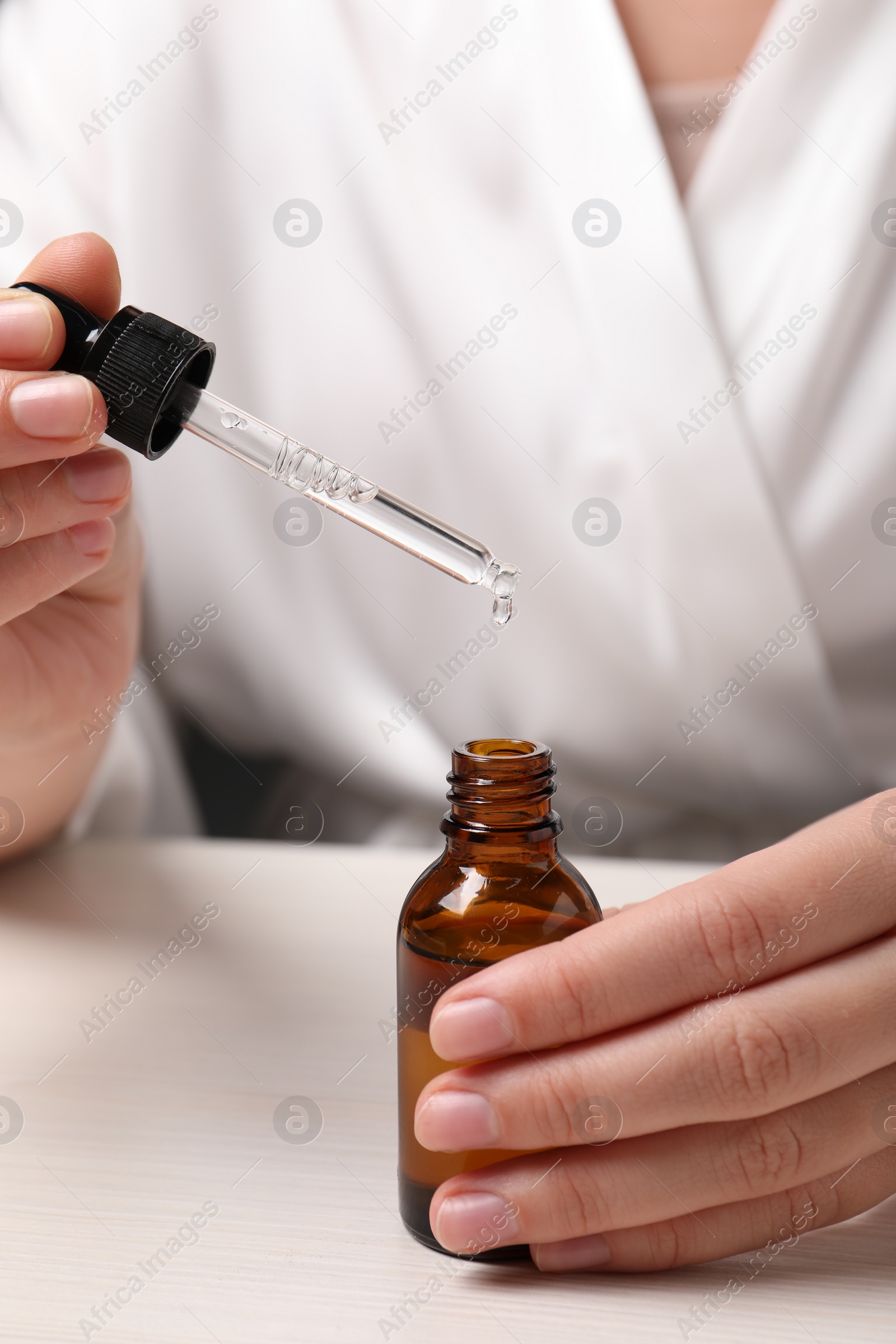 Photo of Woman with bottle of cosmetic serum and pipette at white table, closeup