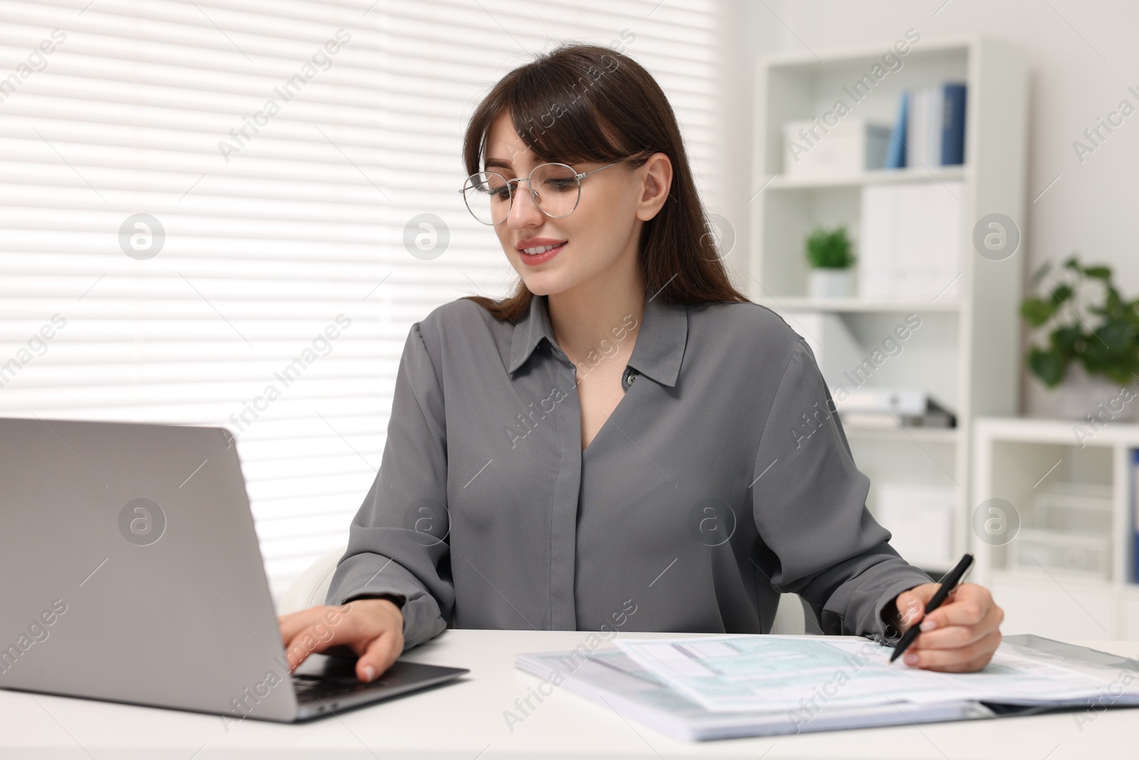 Photo of Smiling secretary doing paperwork at table in office