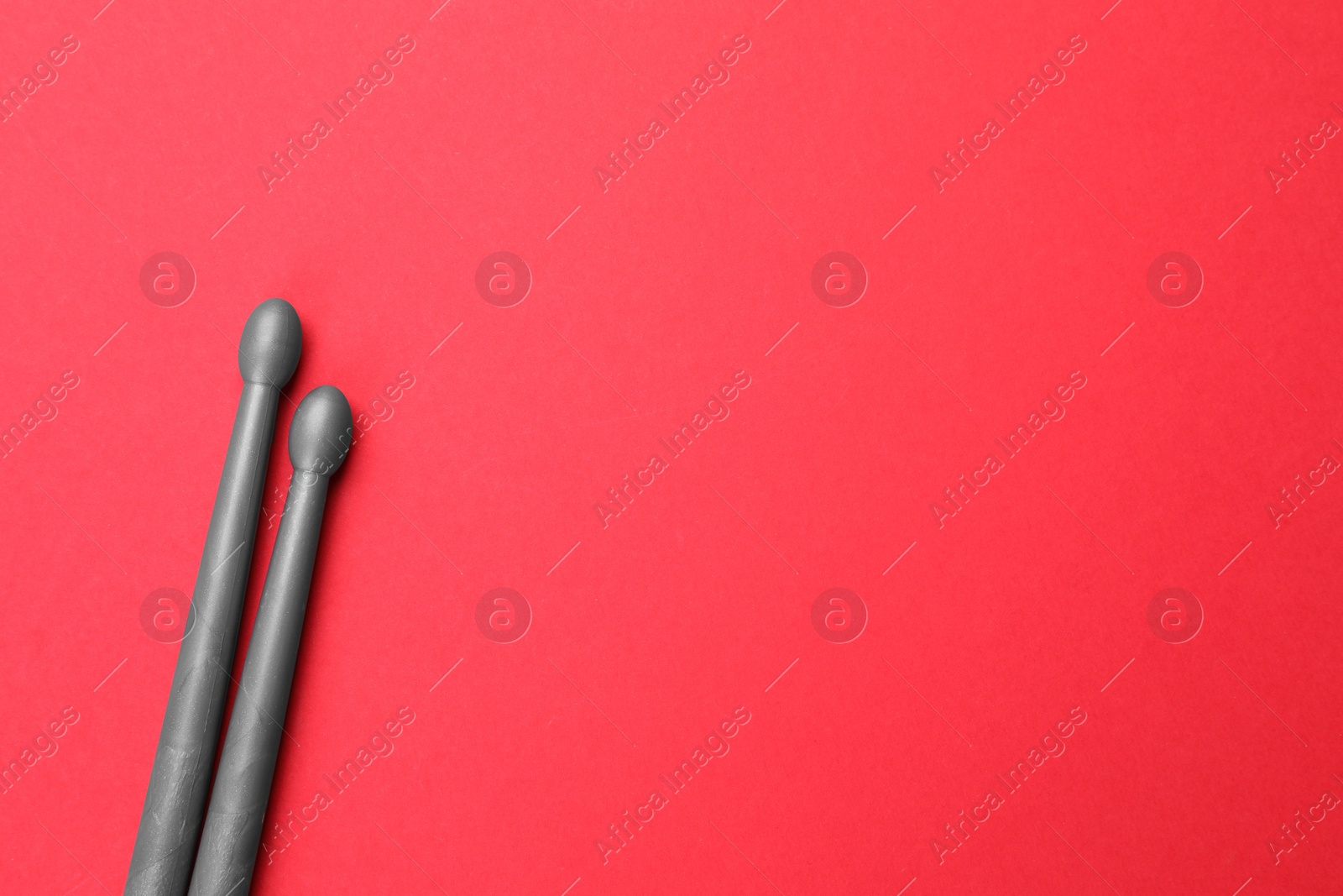 Photo of Two gray drum sticks on red background, top view. Space for text