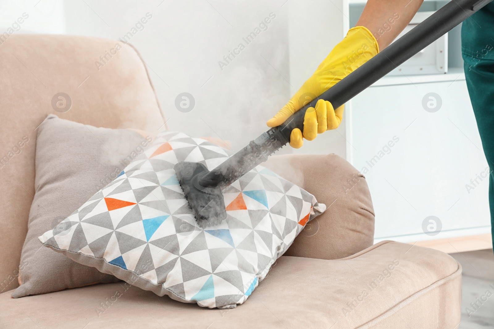 Photo of Janitor removing dirt from sofa cushion with steam cleaner, closeup