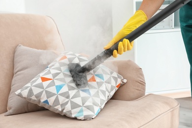 Photo of Janitor removing dirt from sofa cushion with steam cleaner, closeup
