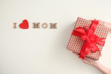 Photo of Phrase I LOVE MOM and child with gift box for Mother's Day on light background, top view