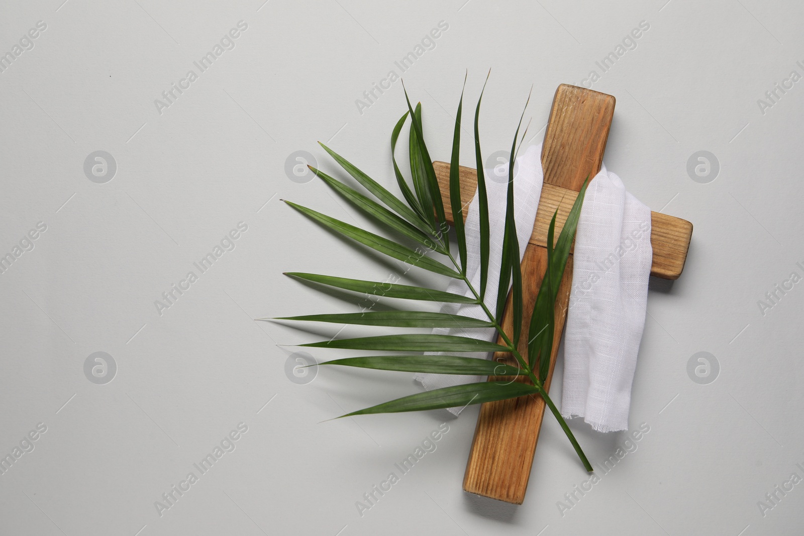 Photo of Wooden cross, white cloth and palm leaf on light grey background, top view with space for text. Easter attributes