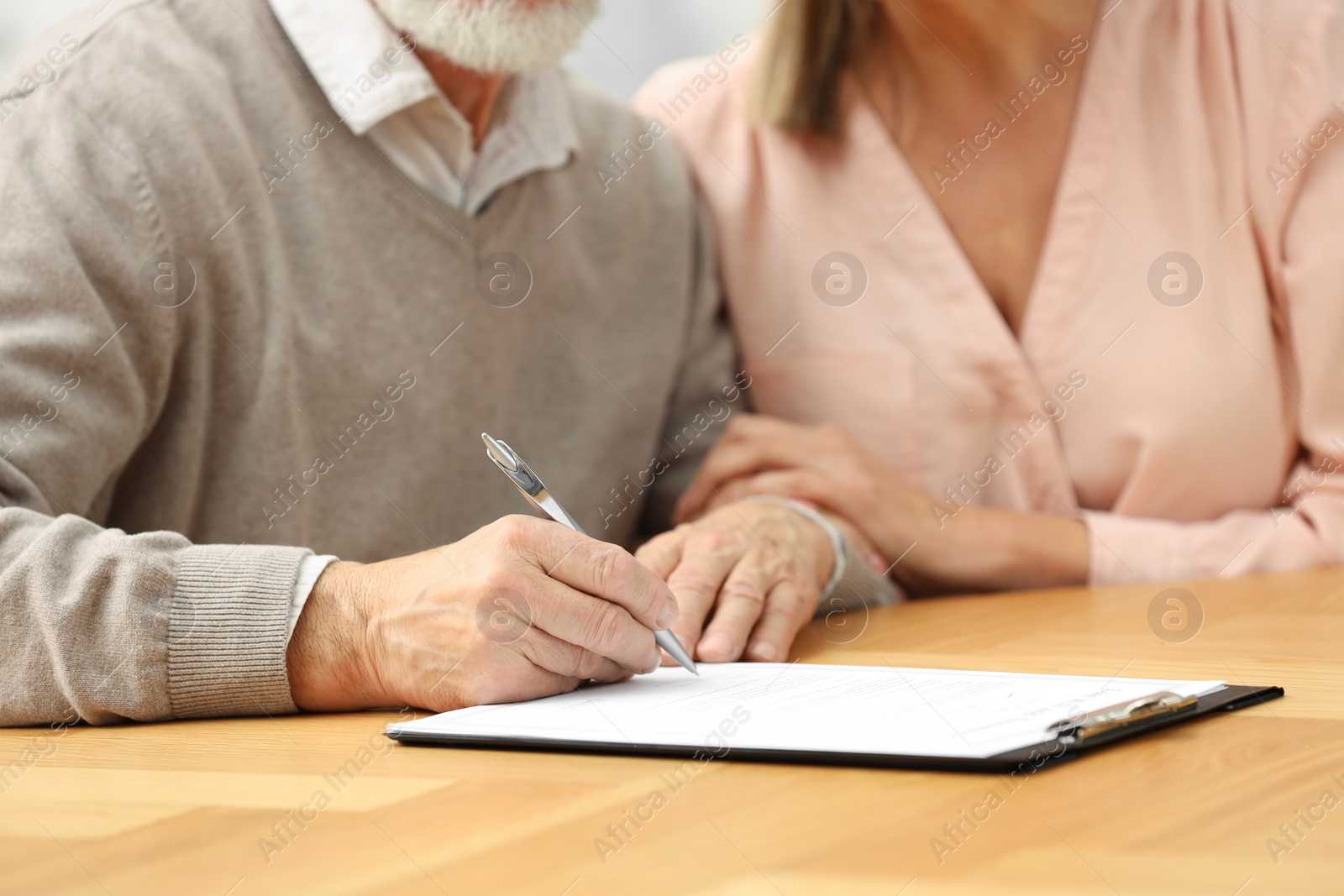 Photo of Senior couple signing Last Will and Testament at wooden table, closeup