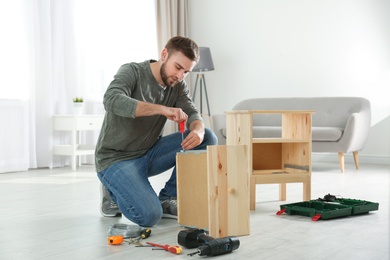 Photo of Young working man repairing drawer at home