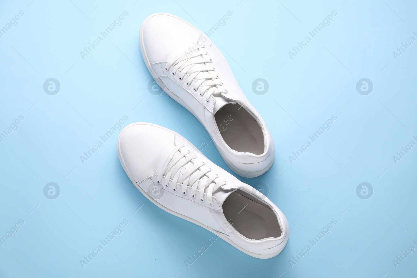 Photo of Pair of stylish white sneakers on light blue background, top view