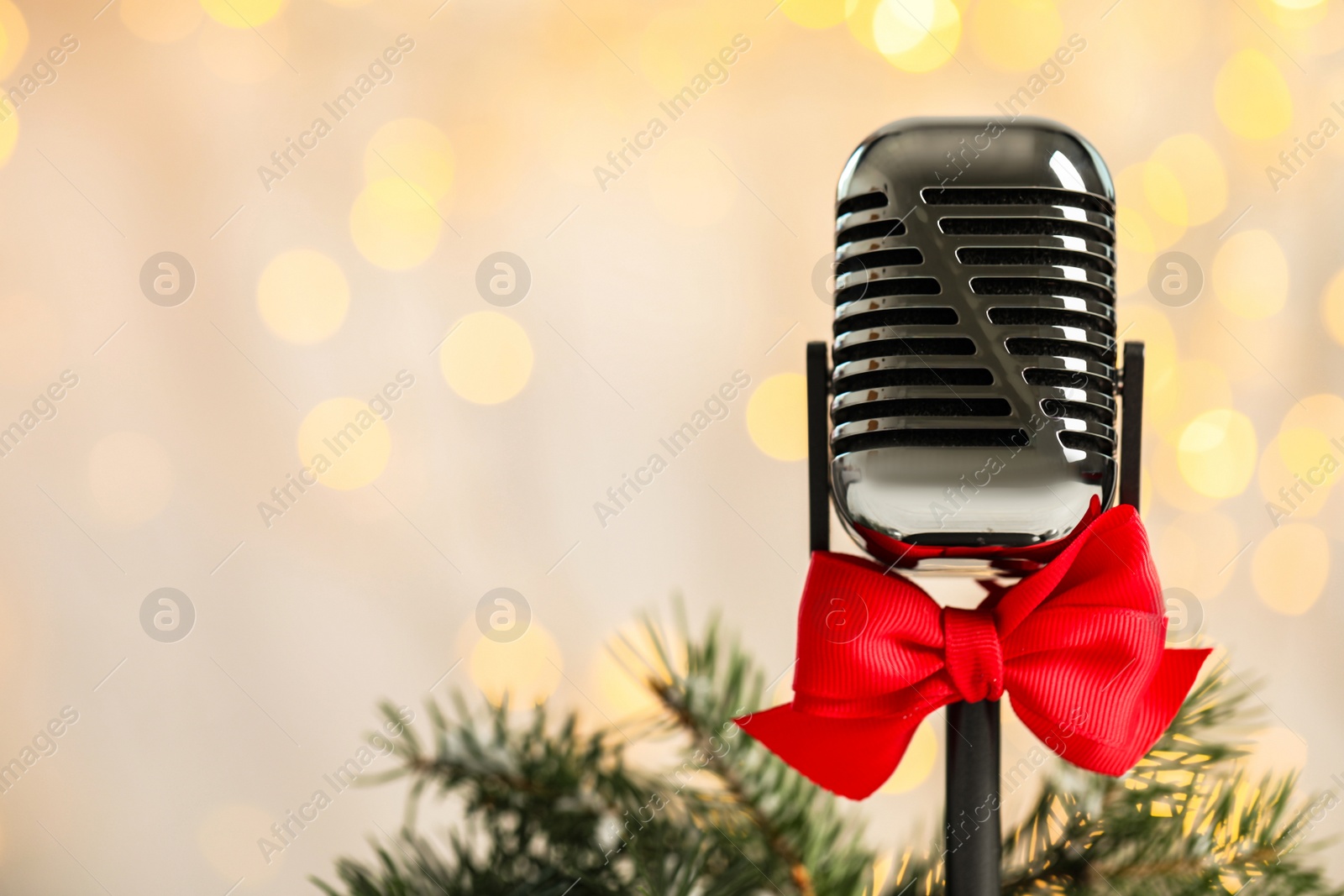 Photo of Microphone with red bow and fir branches against blurred lights, space for text. Christmas music