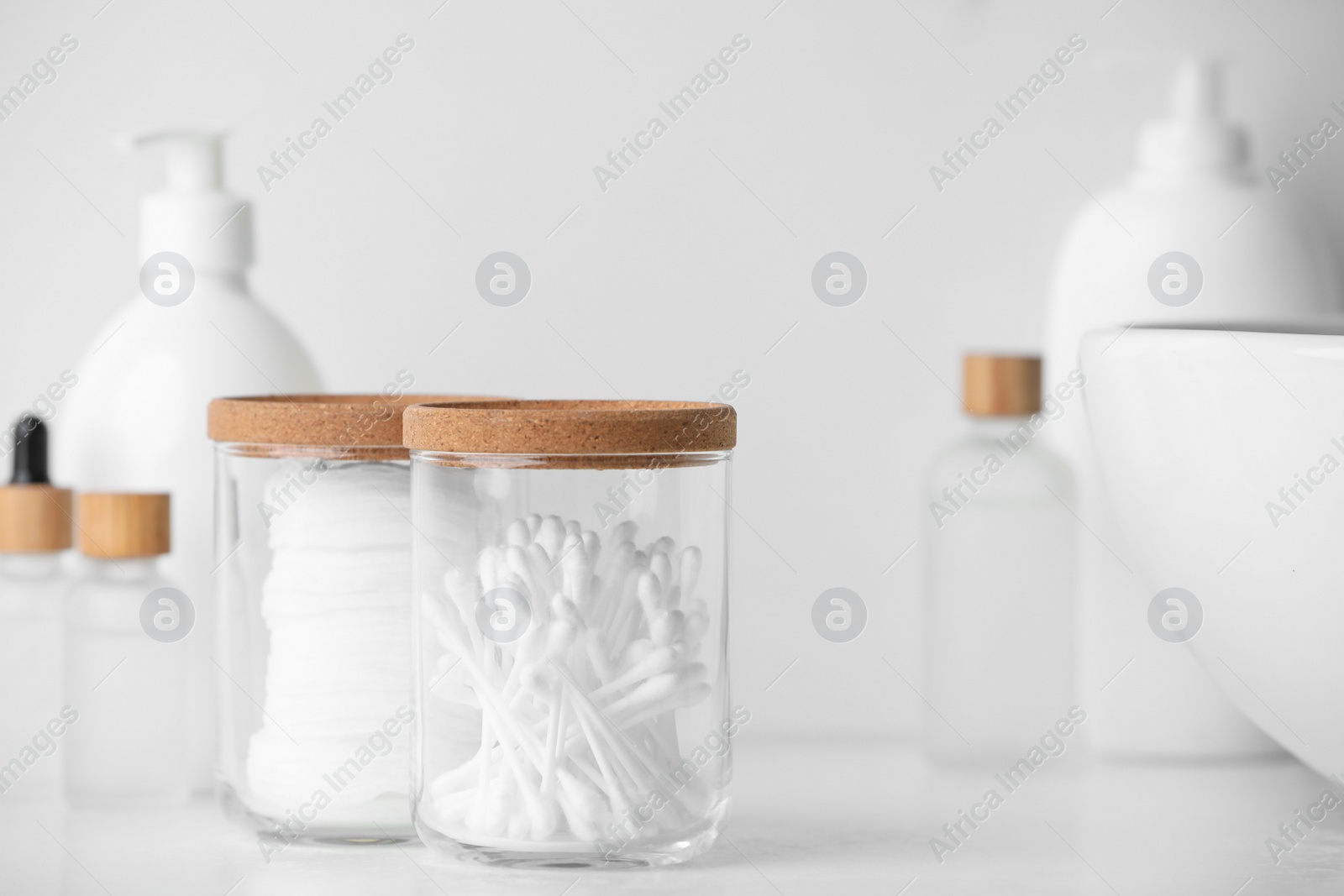 Photo of Glass jars with cotton pads and swabs near cosmetic products on white countertop