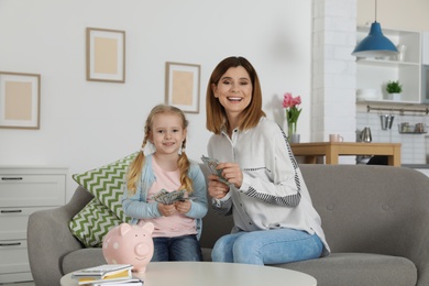 Mother and daughter counting money on sofa indoors