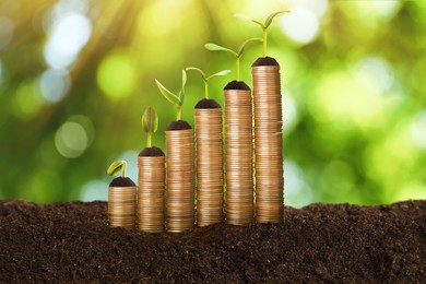 Image of Stacked coins and green seedlings on ground outdoors, bokeh effect. Investment concept