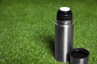 Photo of Modern silver thermos on green grass. Space for text