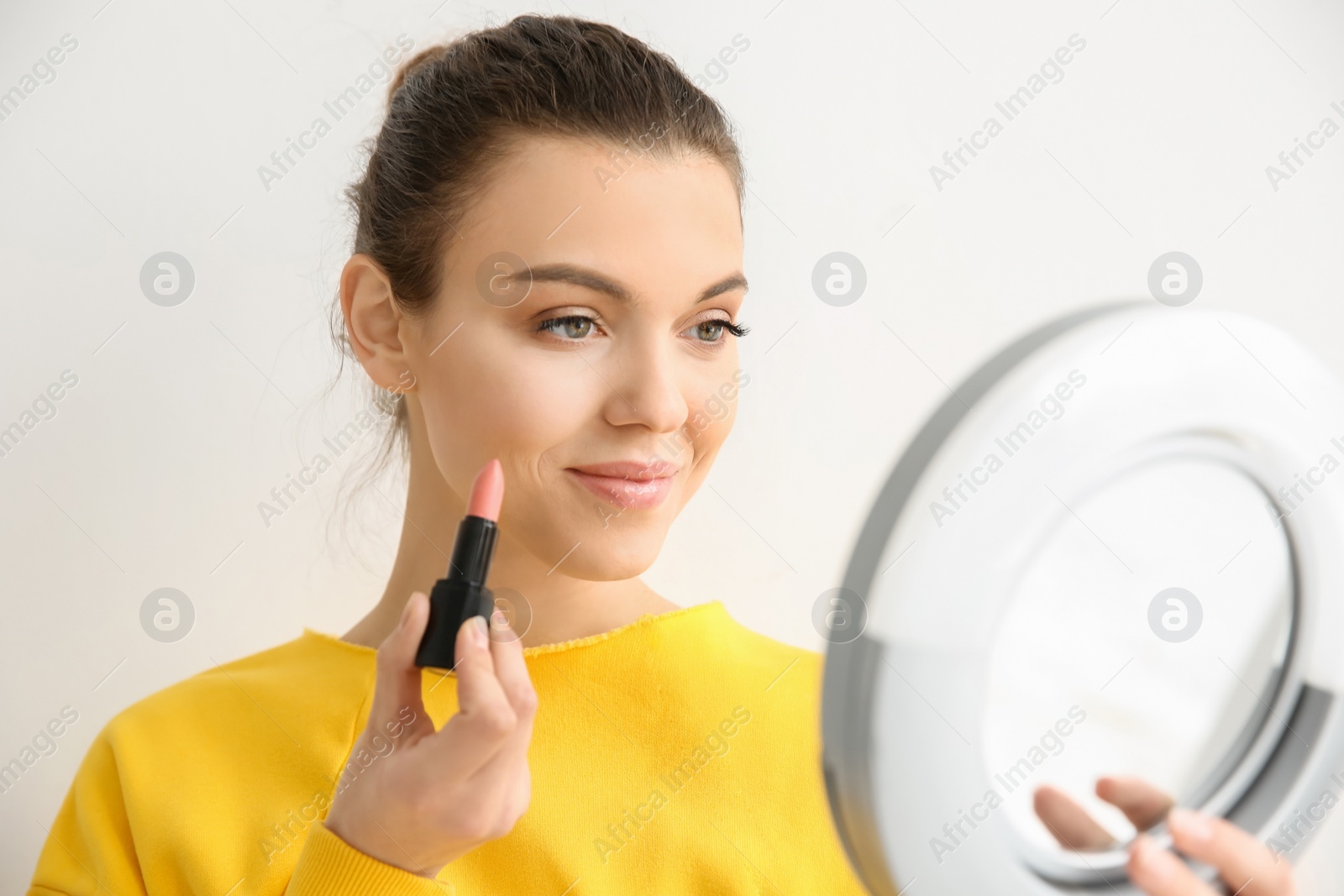 Photo of Young woman applying lipstick on light background. Professional makeup products