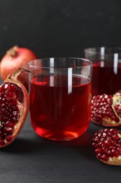 Photo of Tasty pomegranate juice in glasses and fresh fruits on black wooden table, closeup