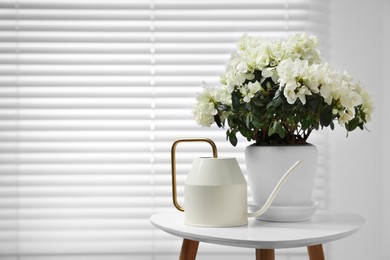 Beautiful azalea plant in flower pot and watering can on white table indoors, space for text