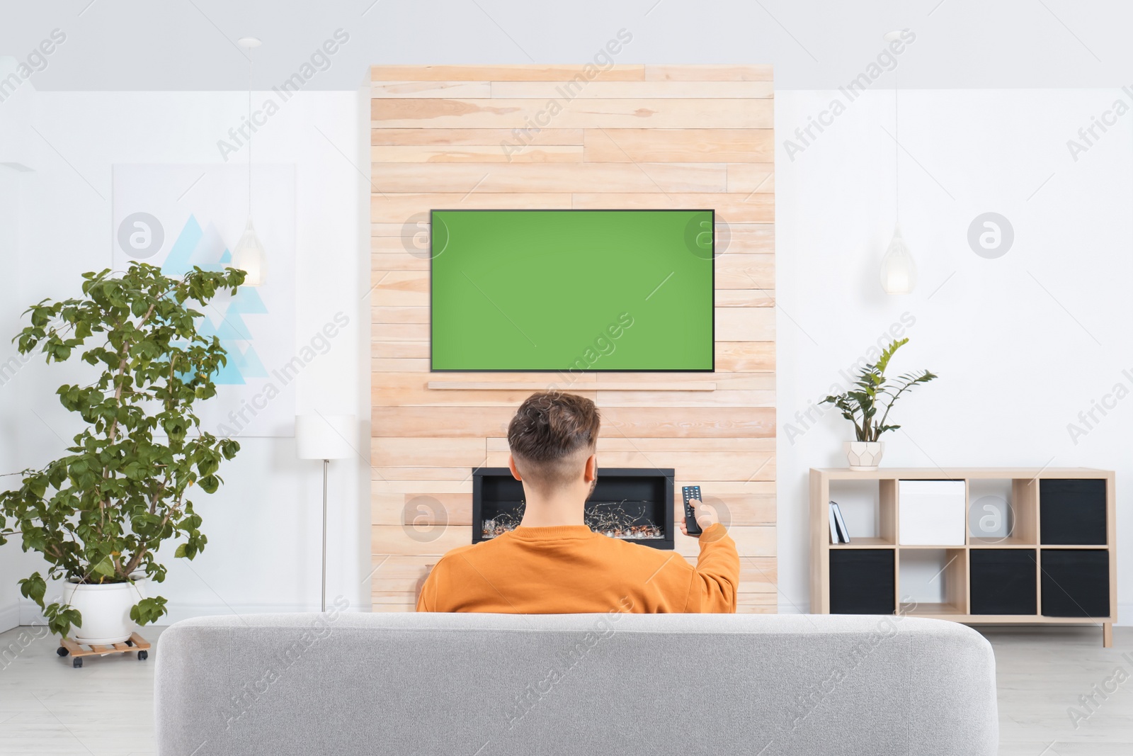 Photo of Man watching TV on sofa in living room with decorative fireplace