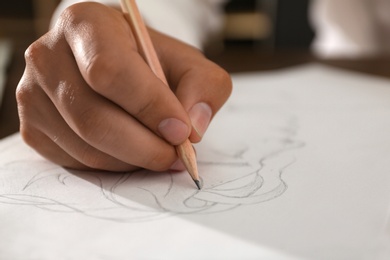 Photo of Man drawing portrait with pencil on sheet of paper, closeup