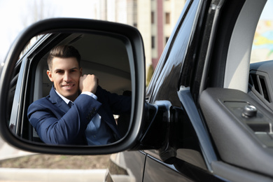 Photo of Handsome man looking into side view mirror of modern car outdoors
