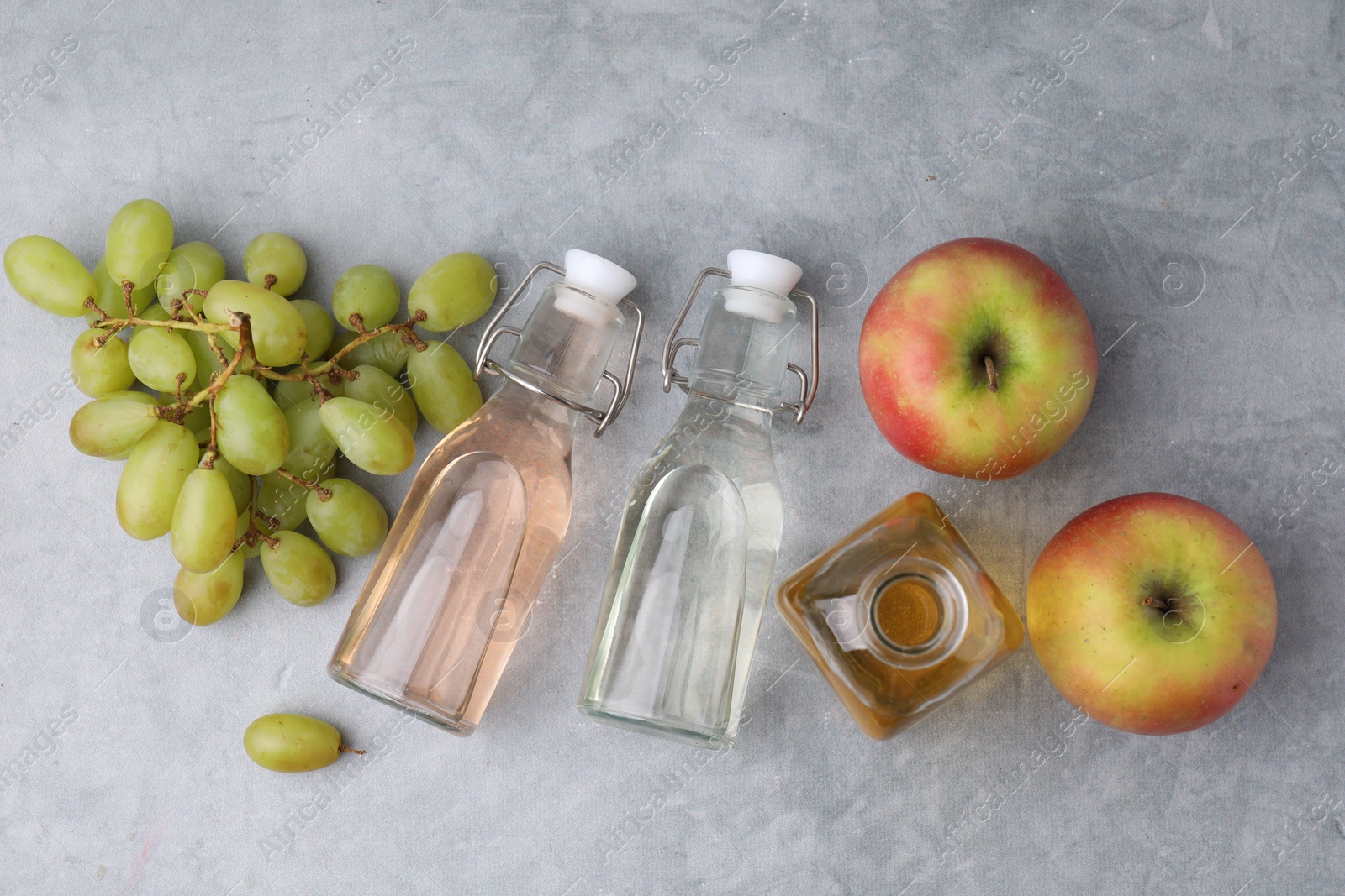 Photo of Different types of vinegar and fresh fruits on grey table, flat lay