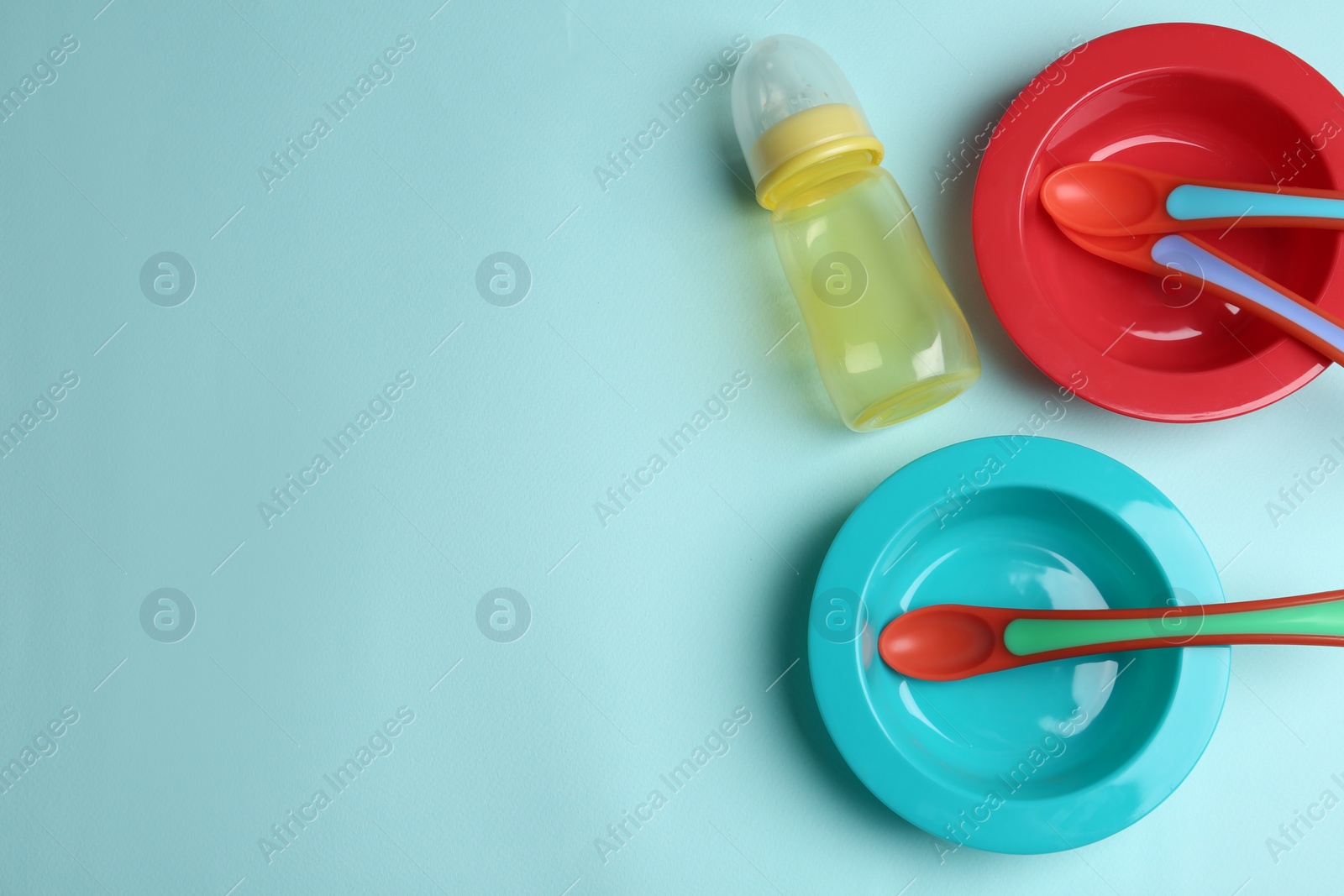 Photo of Set of colorful plastic dishware on light blue background, flat lay with space for text. Serving baby food