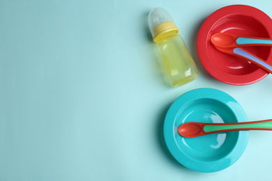 Set of colorful plastic dishware on light blue background, flat lay with space for text. Serving baby food