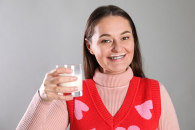 Happy woman with milk mustache holding glass of drink on light grey background