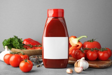 Photo of Bottle of tasty ketchup and ingredients on grey table. Space for text